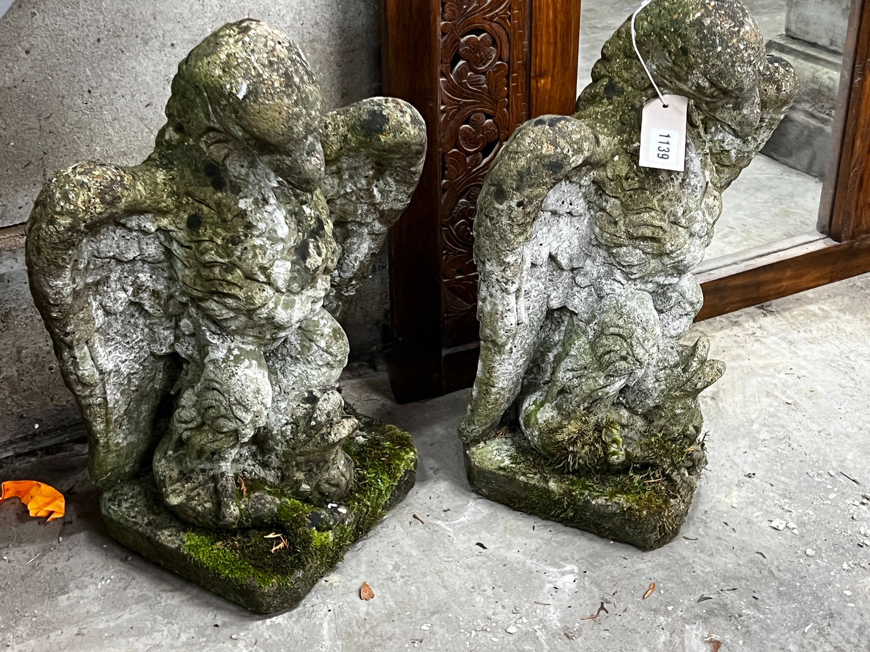 A pair of weathered reconstituted stone eagle and dolphin garden ornaments, height 52cm